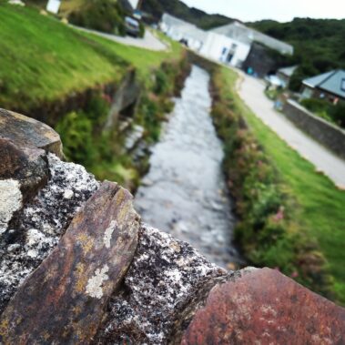Close-up of a stone wall with a small stream and greenery blurred in the background.